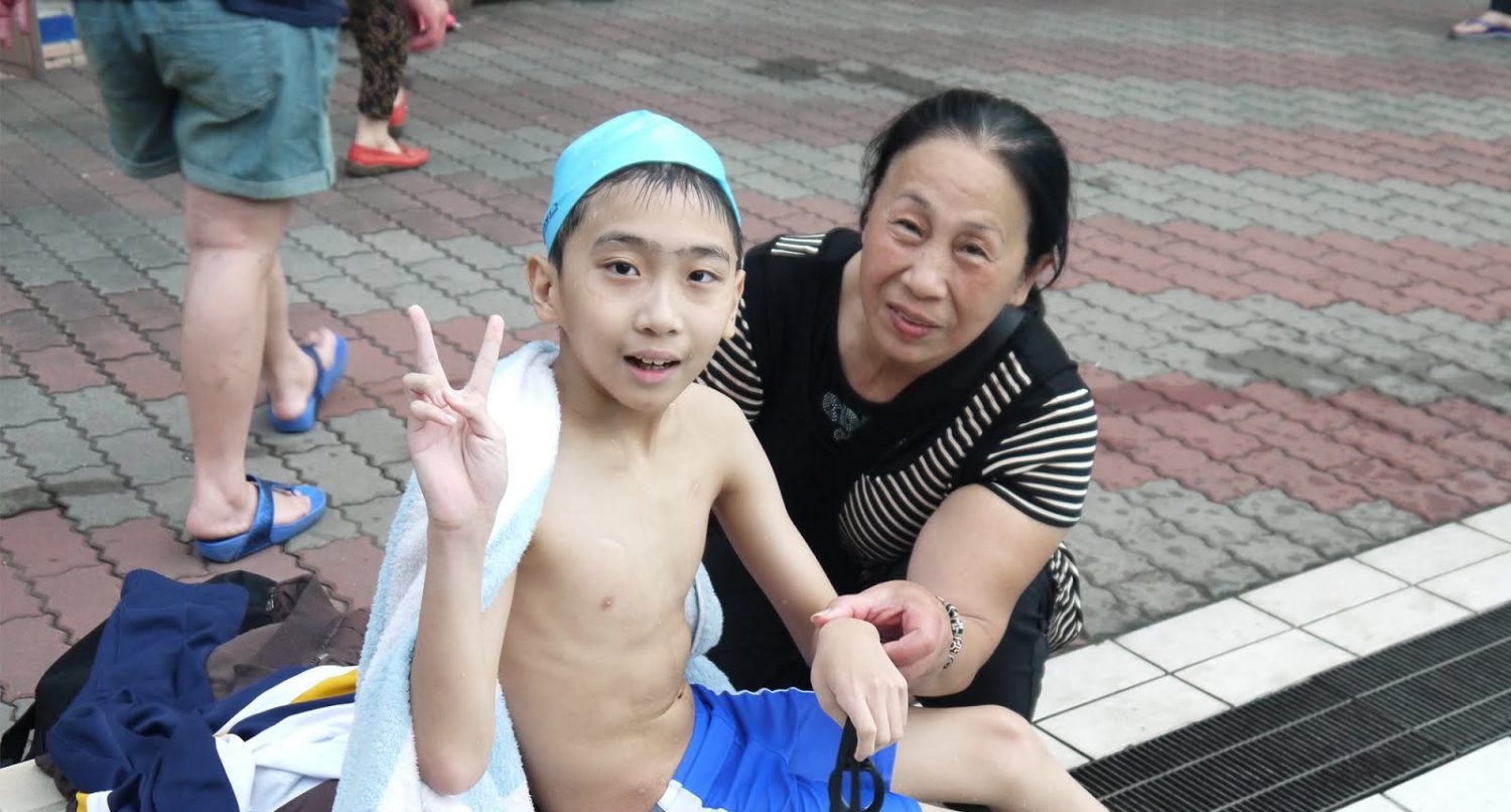 學員賴昱翔(左)因為患有白血病，腳部僵直，最初需由阿嬤(右)抱著來泳池， 透過游泳復健，已經能夠自己走路